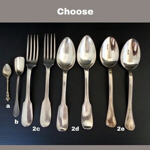 May include: A set of silver cutlery, including a teaspoon, a butter knife, two forks, and three spoons. The spoons are labeled 2c, 2d, and 2e.