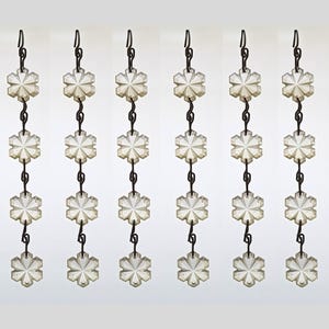 May include: Six vertical strands of clear, faceted glass snowflake ornaments connected by dark metal wire hooks. Each strand features four individual snowflake-shaped crystals arranged in a line, designed for hanging as decorative accents.