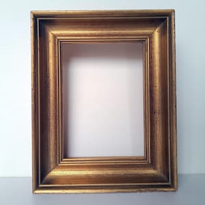 Op de afbeelding: Een rechthoekige, lege fotolijst met een gouden afwerking. De lijst heeft een gedetailleerd, gestructureerd ontwerp en een afgeschuinde rand. De lijst is ontworpen om een foto of kunstwerk in te plaatsen.