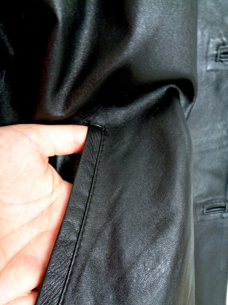 May include: Close-up of a black leather jacket with a zippered pocket and a seam down the side.