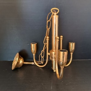 Könnte beinhalten: Ein Vintage-Kronleuchter aus Messing mit drei Kerzenhaltern und einer Mittelsäule. Die Leuchte wird von einer Kette abgehängt und weist ein dekoratives, geschwungenes Design auf. Der Kronleuchter ist etwa 30 cm hoch.