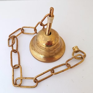 Puede incluir: Una lámpara de techo de latón de estilo vintage, con una pantalla en forma de campana y una cadena a juego. La pantalla tiene un aspecto ligeramente envejecido y los eslabones de la cadena son rectangulares. Diseñada para iluminación cenital.