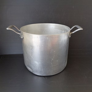 Puede incluir: Una olla grande de aluminio plateado con dos asas. La olla está vacía y tiene una superficie brillante y reflectante.