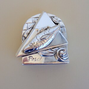 May include: Silver zodiac charm featuring a stylised fish design with the word "Pesci" inscribed below. The charm is in the shape of a triangle with a textured background.