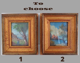 Op de afbeelding: Twee ingelijste landschapschilderijen, een met een groen en blauw landschap en een figuur op de voorgrond, en de andere met een blauw en oranje landschap met een rood gebouw op de achtergrond.