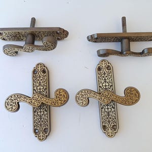 以下が含まれることがあります： 装飾的で渦巻く花の模様が施された、4つのアンティークブロンズドアハンドル。2つのハンドルは、湾曲したレバーが付いた水平方向で、2つは同様のレバーが付いた垂直方向です。ハンドルはおそらく鋳造金属製です。