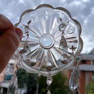 Può includere: Componente di lampadario in vetro trasparente con bordo smerlato e pendenti di cristallo sospesi. Il disco centrale ha un'apertura circolare. Il vetro ha una qualità riflettente e i pendenti sono a forma di goccia.