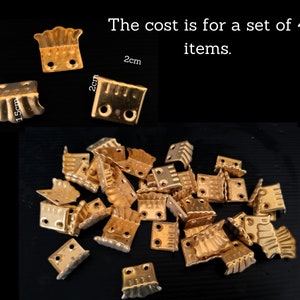 Puede incluir: Una colección de pequeñas escuadras de esquina de metal dorado. Las escuadras miden aproximadamente 1,5 cm por 2 cm. La imagen también incluye el texto "The cost is for a set of 4 items."