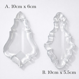 Peut inclure: Deux formes décoratives en acrylique transparent avec un design orné. La première mesure 10 cm x 6 cm, et la seconde mesure 10 cm x 5,5 cm. Les formes sont transparentes et ont une forme symétrique et stylisée, adaptée aux travaux manuels ou à la décoration.