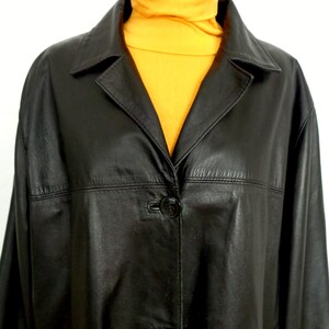 May include: A black leather jacket with a button closure and a collar. The jacket is on a mannequin wearing a yellow turtleneck.