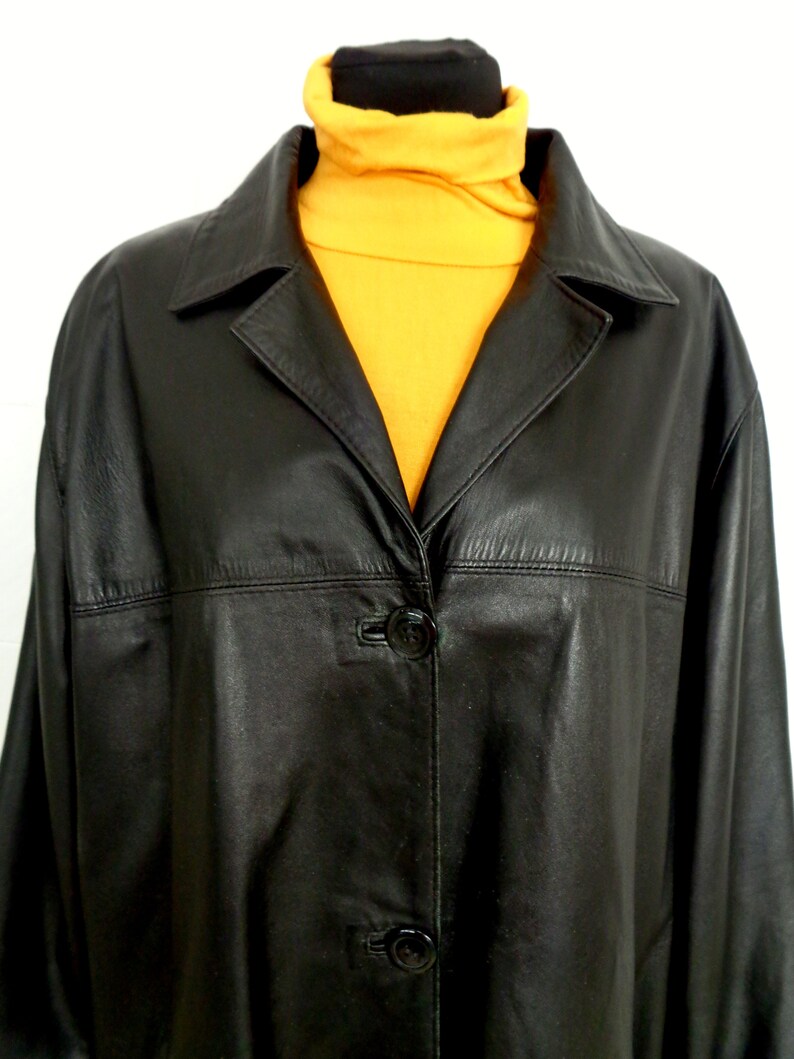 May include: A black leather jacket with a button closure and a collar. The jacket is on a mannequin wearing a yellow turtleneck.