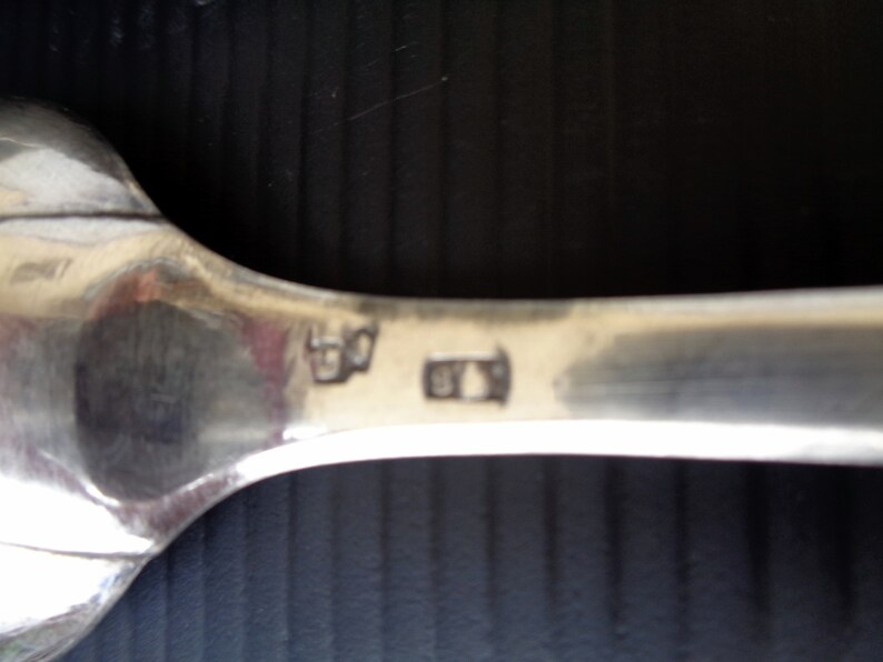 May include: Close-up of the back of a silver spoon with the markings "830" and "815" stamped on the back.