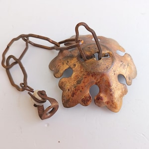 Op de afbeelding: Een antieke bronzen plafondventilator trekketting met een blad-vormig decoratief element. Het blad heeft een verweerde, verouderde uitstraling met een ketting en katrol bevestigd. Het algehele ontwerp is vintage.