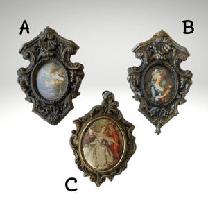 Puede incluir: Tres marcos de fotos ovalados de estilo antiguo con bordes ornamentados de color bronce. Cada marco presenta una pintura en miniatura en su interior. Los marcos están etiquetados A, B y C. Las pinturas representan escenas y figuras clásicas.