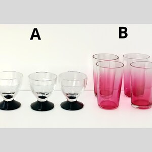 May include: A collection of glassware, including three clear stemmed glasses with black bases and four tall glasses with a pink ombre effect. The glasses are arranged on a white surface against a white background.