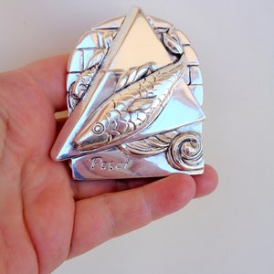 May include: Silver zodiac pendant featuring a stylised fish design with the word "Pisces" inscribed below. The pendant is in the shape of a triangle with a textured background.