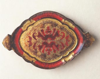 May include: An oval-shaped decorative tray featuring a vibrant red and metallic gold finish. The center displays an intricate, symmetrical floral pattern in red against a gold background, surrounded by a red border and scalloped edges.