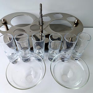 May include: A silver-toned serving set with a central handle and two oval trays with circular cutouts. It includes six clear shot glasses and two clear glass dishes, perfect for serving appetizers or drinks.