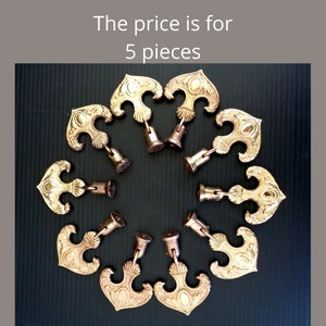 May include: A collection of ten ornate, gold-colored decorative hardware pieces arranged in a circular pattern. Each piece has a stylized, symmetrical design with a central oval and curved edges. The text "The price is for 5 pieces" is visible.