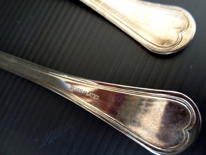 May include: Two silver-plated spoons with heart-shaped ends. The spoons are marked "SILVER PLATED" on the back.