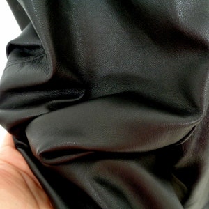 May include: Close-up of black leather fabric with a textured surface. The fabric is folded and shows wrinkles.