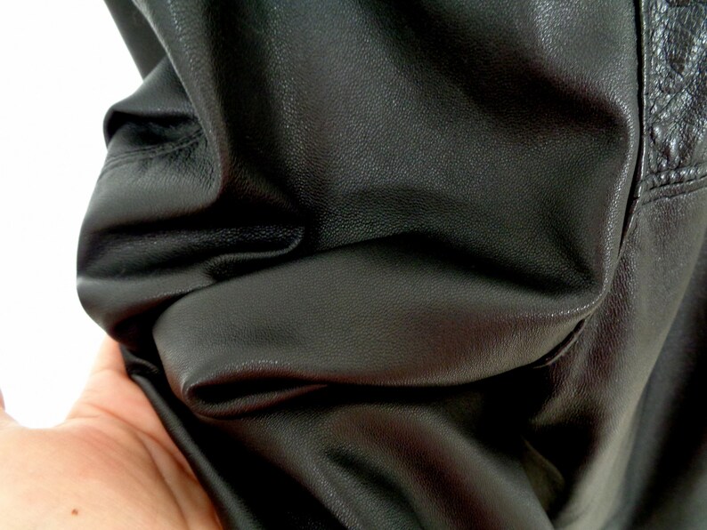 May include: Close-up of black leather fabric with a textured surface. The fabric is folded and shows wrinkles.