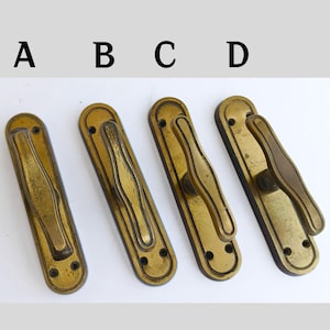 May include: Four antique brass door handles, each with a unique design. The handles are labeled A, B, C, and D. Each handle has a rectangular backplate with a decorative handle. The brass has a warm, aged patina.