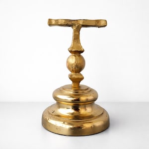 May include: A gold-colored, decorative pedestal with a T-shaped top. The pedestal has a round base and a central sphere, all with a metallic finish. The design is ornate and vintage-inspired, suitable for displaying small items.