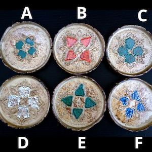 Könnte beinhalten: Sechs handgefertigte Keramikuntersetzer mit metallisch goldener Oberfläche und verschiedenen farbenfrohen floralen Designs. Die Untersetzer haben türkisfarbene, rote, weiße und blaue Akzente. Jeder Untersetzer hat einen Durchmesser von etwa 10 cm.