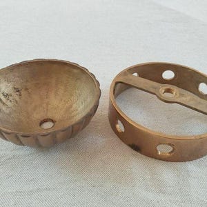 May include: A brass ceiling canopy and a matching circular mounting bracket. The canopy is bowl-shaped with a fluted exterior and a central hole. The mounting bracket is a flat ring with side holes and a central threaded opening for installation.