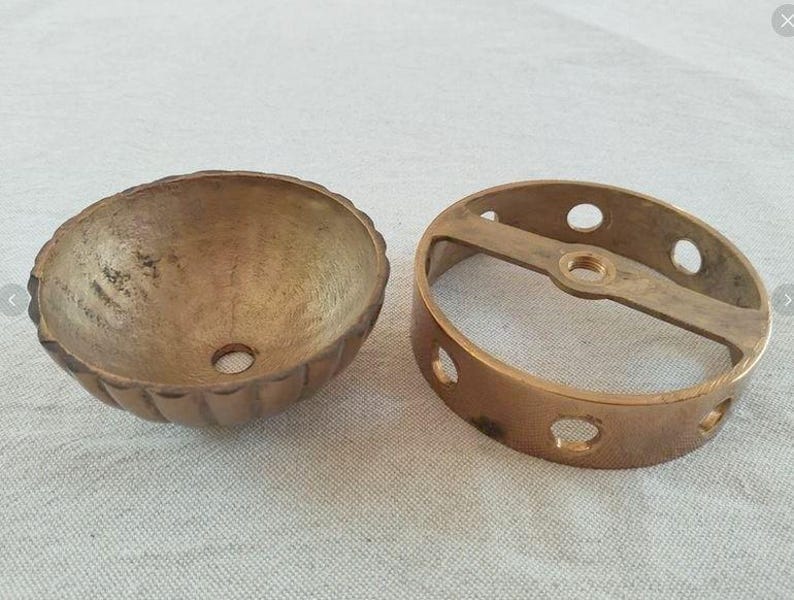 May include: A brass ceiling canopy and a matching circular mounting bracket. The canopy is bowl-shaped with a fluted exterior and a central hole. The mounting bracket is a flat ring with side holes and a central threaded opening for installation.