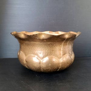 May include: A hammered brass planter with a scalloped rim. The planter has a rounded body with a textured surface and a warm, metallic finish. The design is reminiscent of a flower.
