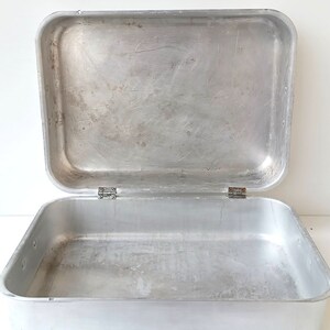 Op de afbeelding: Een rechthoekige bakvorm van zilverkleurig aluminium met een deksel. De vorm is leeg en heeft een licht verweerd oppervlak.