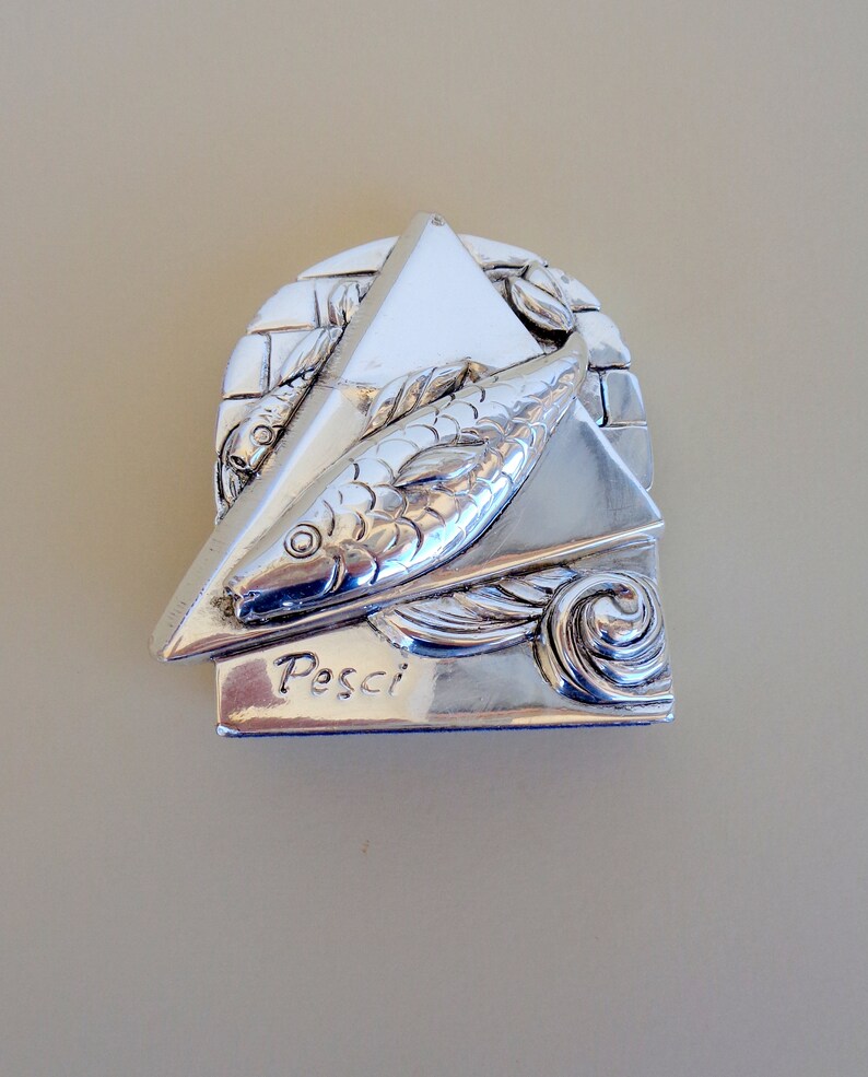 May include: Silver zodiac charm featuring a stylised fish design with the word "Pesci" inscribed below. The charm is in the shape of a triangle with a textured background.