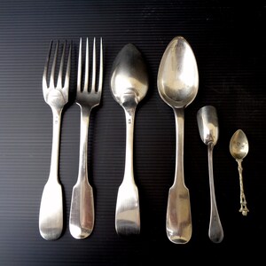 May include: A set of six silver-plated utensils, including two forks, two spoons, and two teaspoons. The utensils are arranged in a row on a black surface.