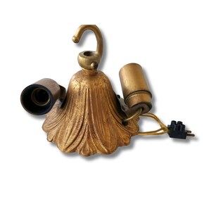 May include: A vintage gold ceiling light fitting with two bulb holders and a hook. The fitting has a decorative, scalloped base and exposed wiring with a black plug.