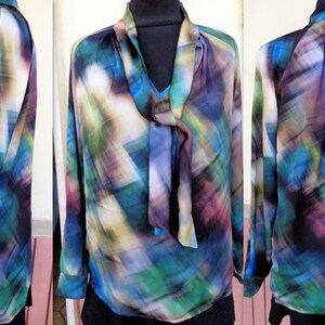 May include: A long-sleeved blouse with a colorful abstract pattern in shades of blue, green, purple, and white. The blouse features a tie-neck design and is made of a lightweight, flowing fabric. The garment is displayed on a mannequin.