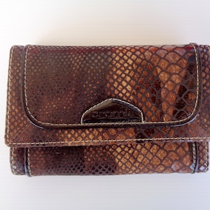 Op de afbeelding: Een bruine leren portemonnee met een slangenhuidpatroon en het woord "Cromie" erop gegraveerd.