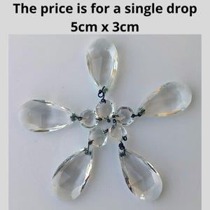 Op de afbeelding: Heldere kristallen kroonluchterdruppels gerangschikt in een stervormig patroon. Elke druppel is ongeveer 5 cm bij 3 cm. De druppels zijn verbonden met kleine, ronde kristallen en donker draad. Tekst op de afbeelding luidt: "The price is for a single drop 5cm x 3cm."