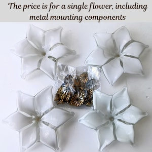 May include: Four white glass flower-shaped decorative pieces with a star-like design. A clear plastic bag contains small, gold-colored metal mounting components. The text at the top reads: "The price is for a single flower, including metal mounting components."