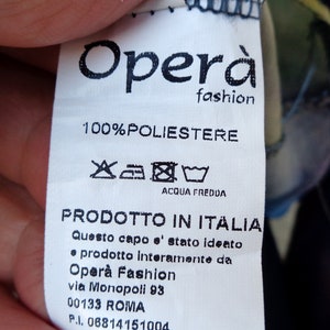 May include: A white clothing tag with the text "Opera fashion" and "100% POLIESTERE". The tag also includes washing instructions and the text "PRODOTTO IN ITALIA".