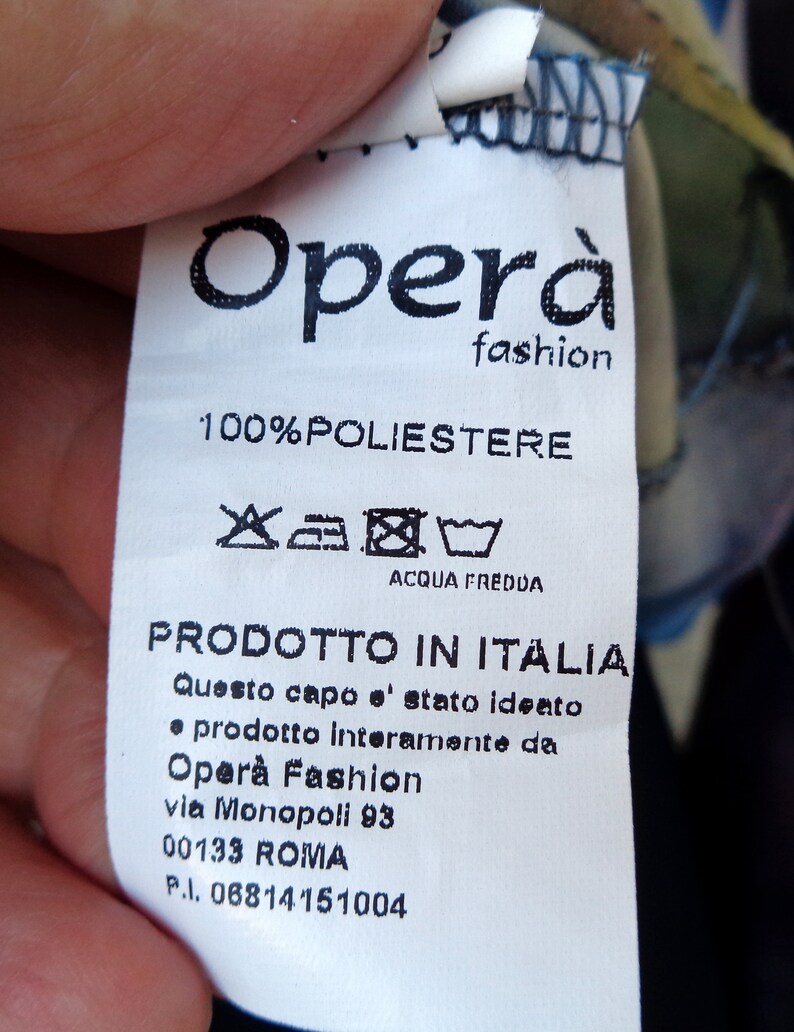 May include: A white clothing tag with the text "Opera fashion" and "100% POLIESTERE". The tag also includes washing instructions and the text "PRODOTTO IN ITALIA".