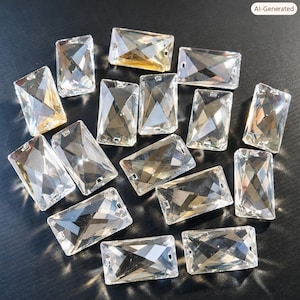 May include: A collection of clear, rectangular glass crystals with faceted surfaces. Each piece features two small holes on opposite ends, designed for attachment. The crystals are arranged in a scattered pattern, reflecting light across their edges.