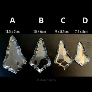 Op de afbeelding: Vier heldere kristallen kroonluchterhangers in verschillende maten en vormen. Afmetingen: 11,5 x 7 cm, 10 x 6 cm, 9 x 5,5 cm en 7,5 x 5 cm. De hangers worden getoond tegen een donkere achtergrond.