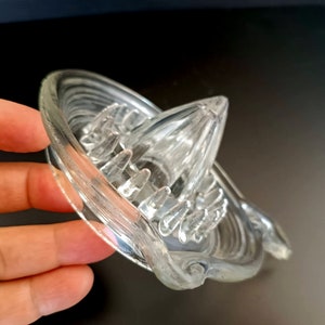 Op de afbeelding: Een heldere glazen citruspers met een geribbelde ruimer en een schenktuit. De pers heeft een kegelvormig middenstuk voor het persen van citrusvruchten en een reeks ribbels om pitten op te vangen. Het ontwerp is eenvoudig en functioneel.