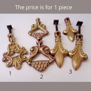 Puede incluir: Primer plano de cinco tiradores de cajón antiguos de latón con diseños ornamentados. Cada tirador tiene un tornillo de metal oscuro y un frente decorativo. La imagen incluye el texto "The price is for 1 piece" y los números 1, 2 y 3.