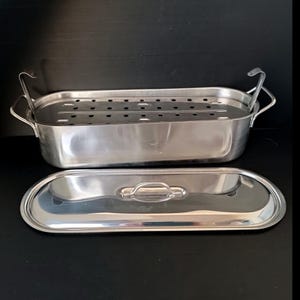 May include: Stainless steel fish steamer with a perforated insert and a matching lid. The oval-shaped steamer has handles on the sides and the lid has a single handle. The set is designed for steaming fish and other foods.