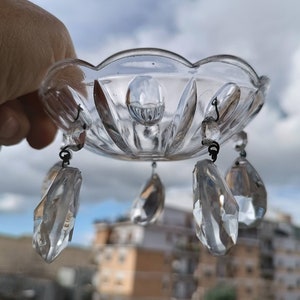 Può includere: Componente di lampadario in vetro trasparente con bordo smerlato e pendenti di cristallo. Il vetro ha un design sfaccettato e i pendenti sono a forma di goccia. Sfondo di cielo nuvoloso.