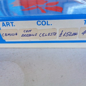 May include: A blue box with white labels that say "ART. CAMICIA CON BREDELLA CELESTE L 150.000 46"
