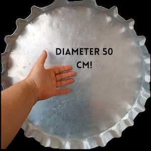 May include: A large, silver metal bottle cap with a crimped edge. The text "DIAMETER 50 CM!" is printed on the cap. The diameter is approximately 19.6 inches. The cap is set against a black background.